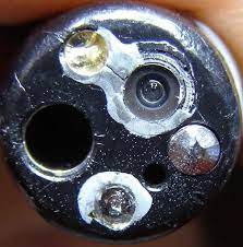 Close-up of a reusable endoscope tip showing debris and discolouration around the lens and light-post recesses